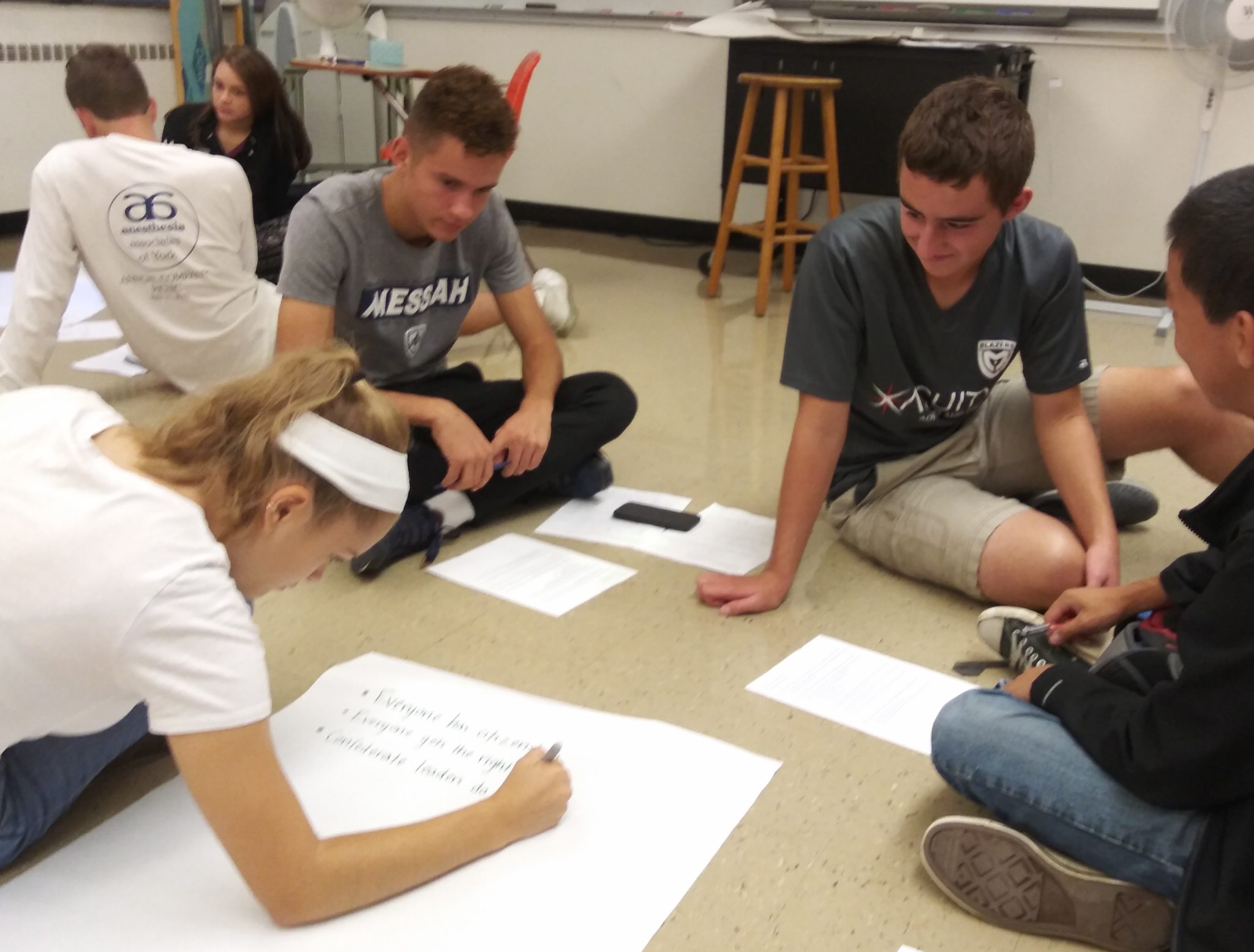 Students collaborating on a class project, drawing on paper on the floor