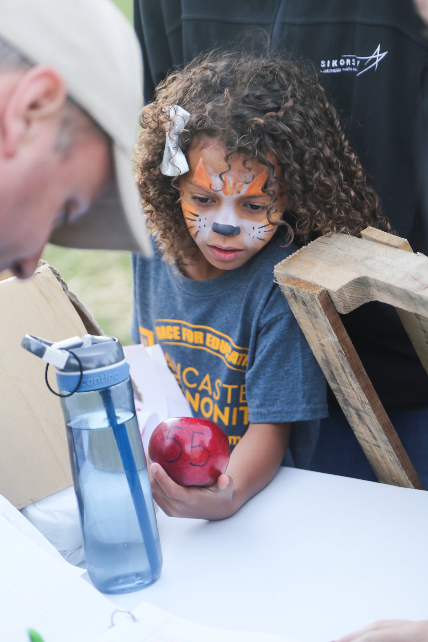 student with tiger face painting holding an apple