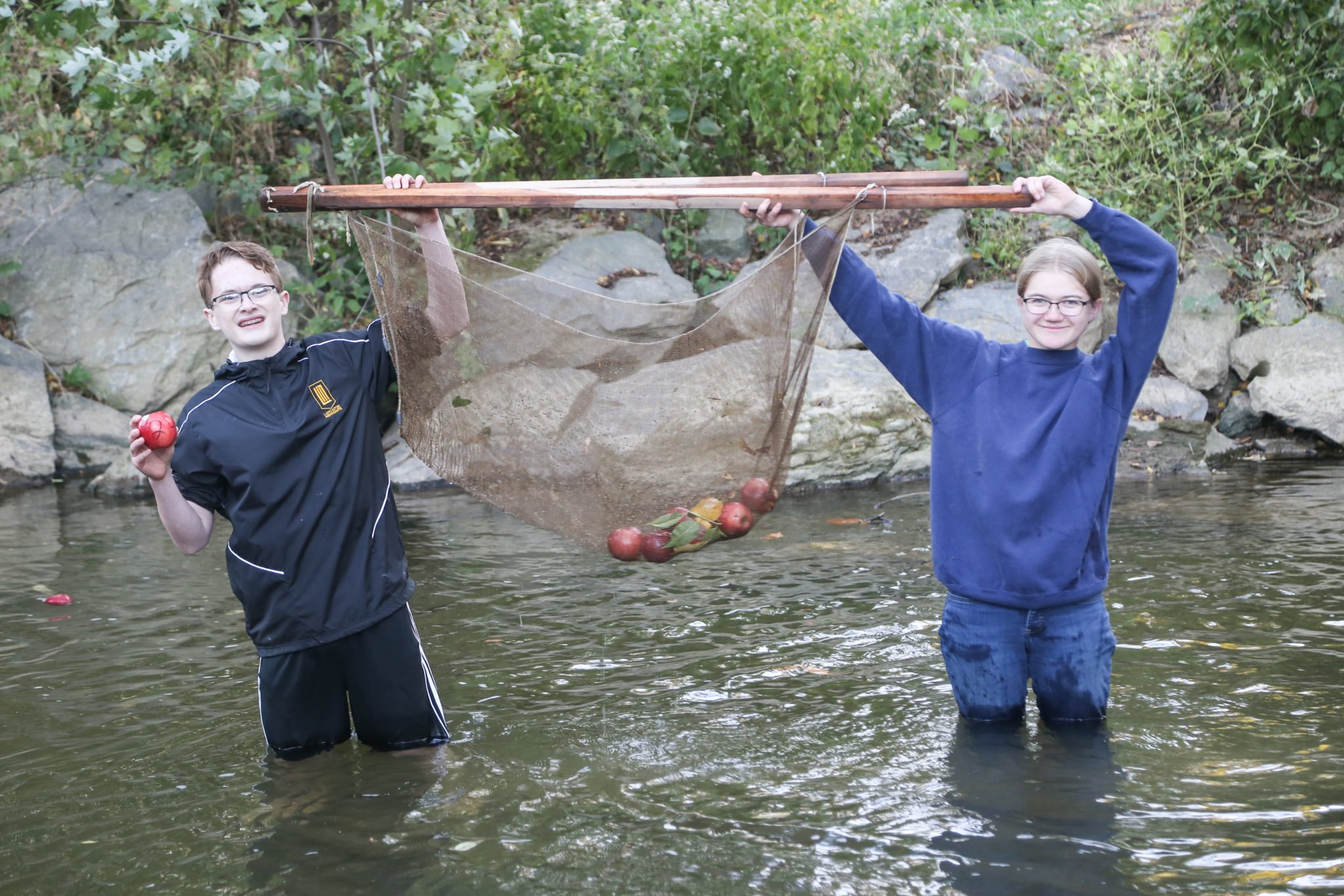 students standing in millstream creek holding a net with apples in it