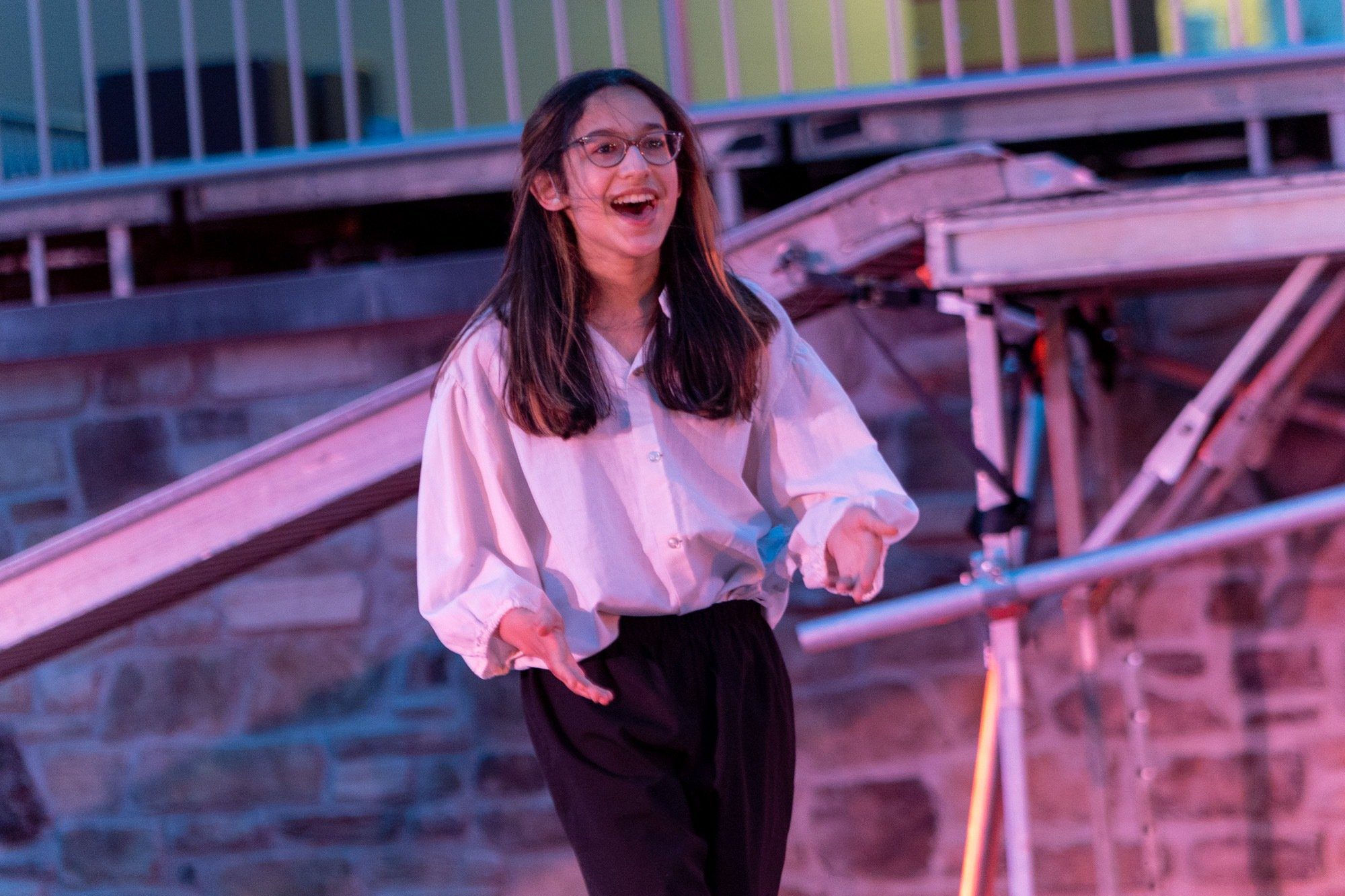 student smiling during the performance of all the worlds a stage