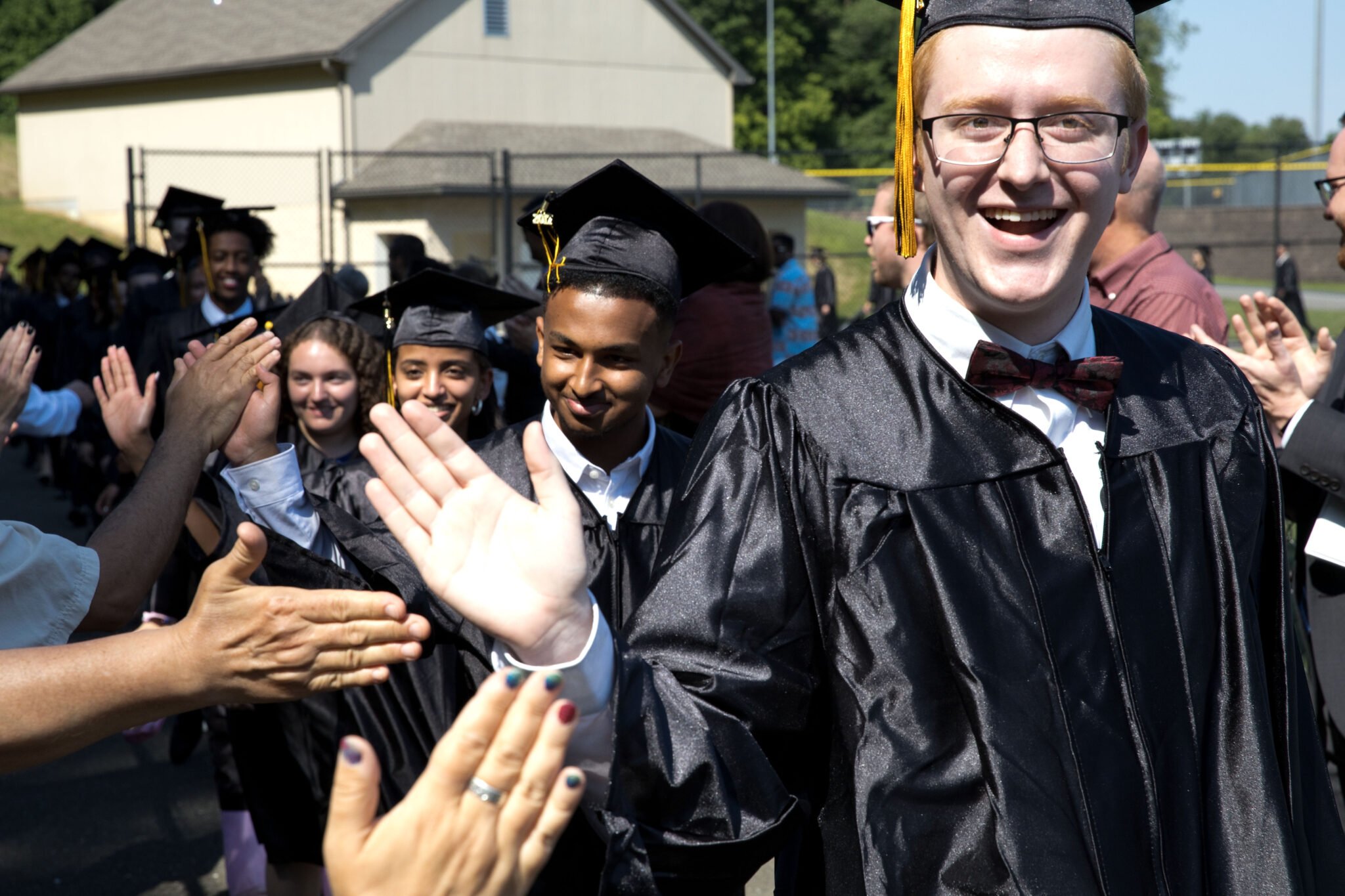 graduates walking into commencement high fiving teachers