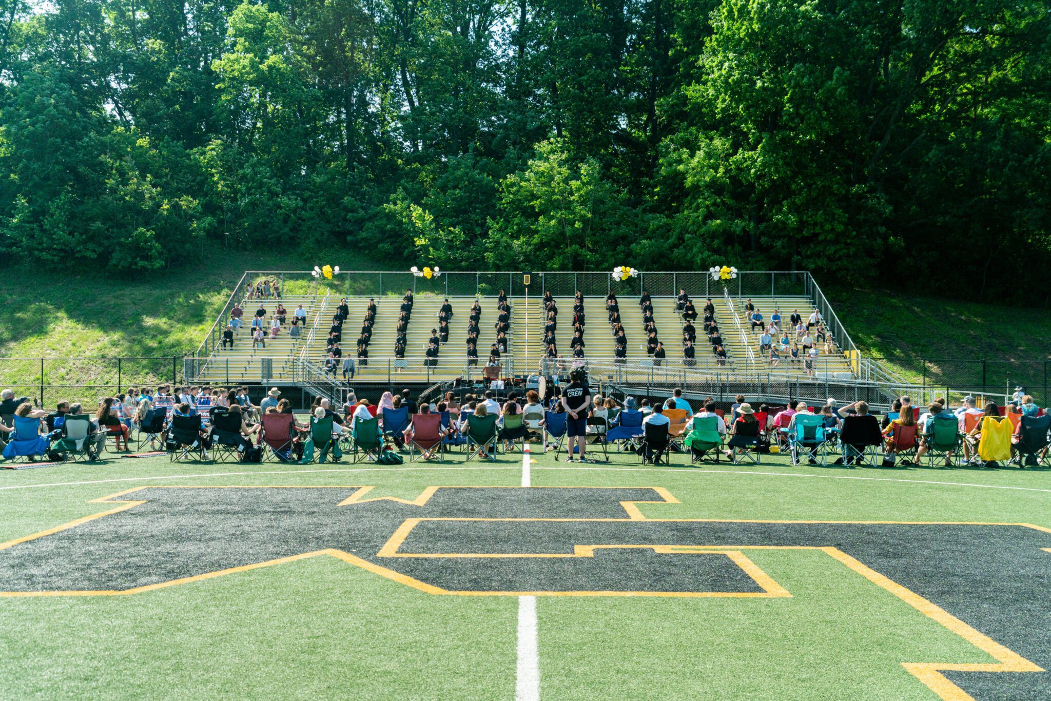 wide angle look at graduation on turf field with bleachers in back