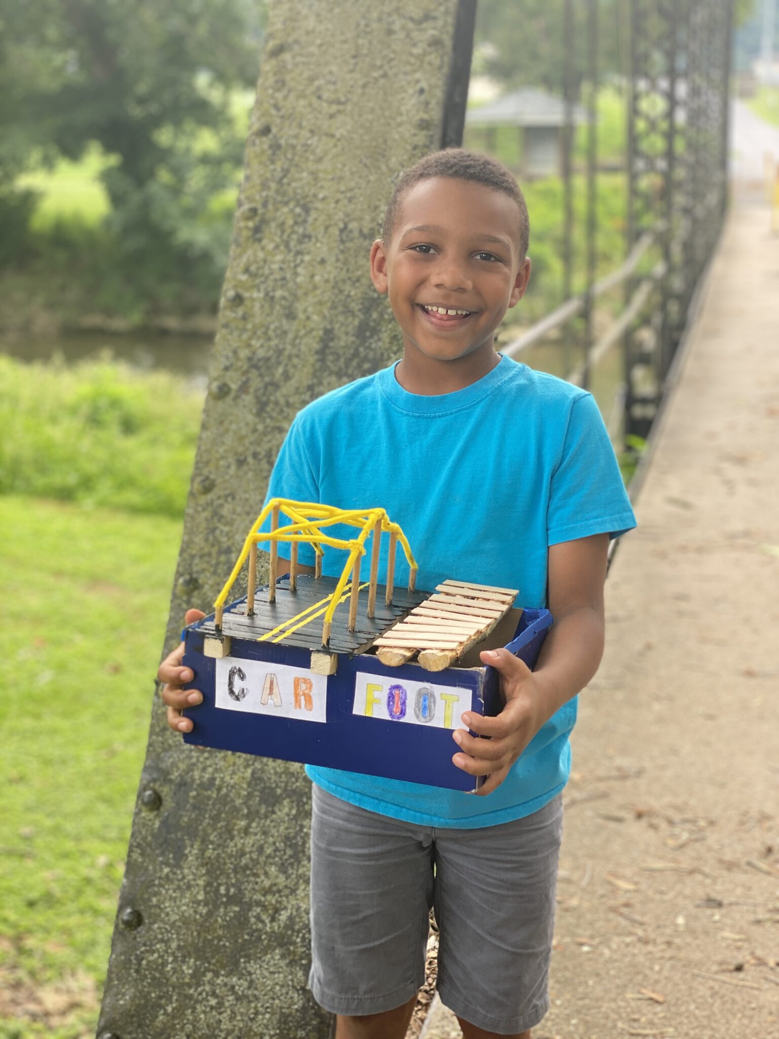 student outside holds bridge art creation