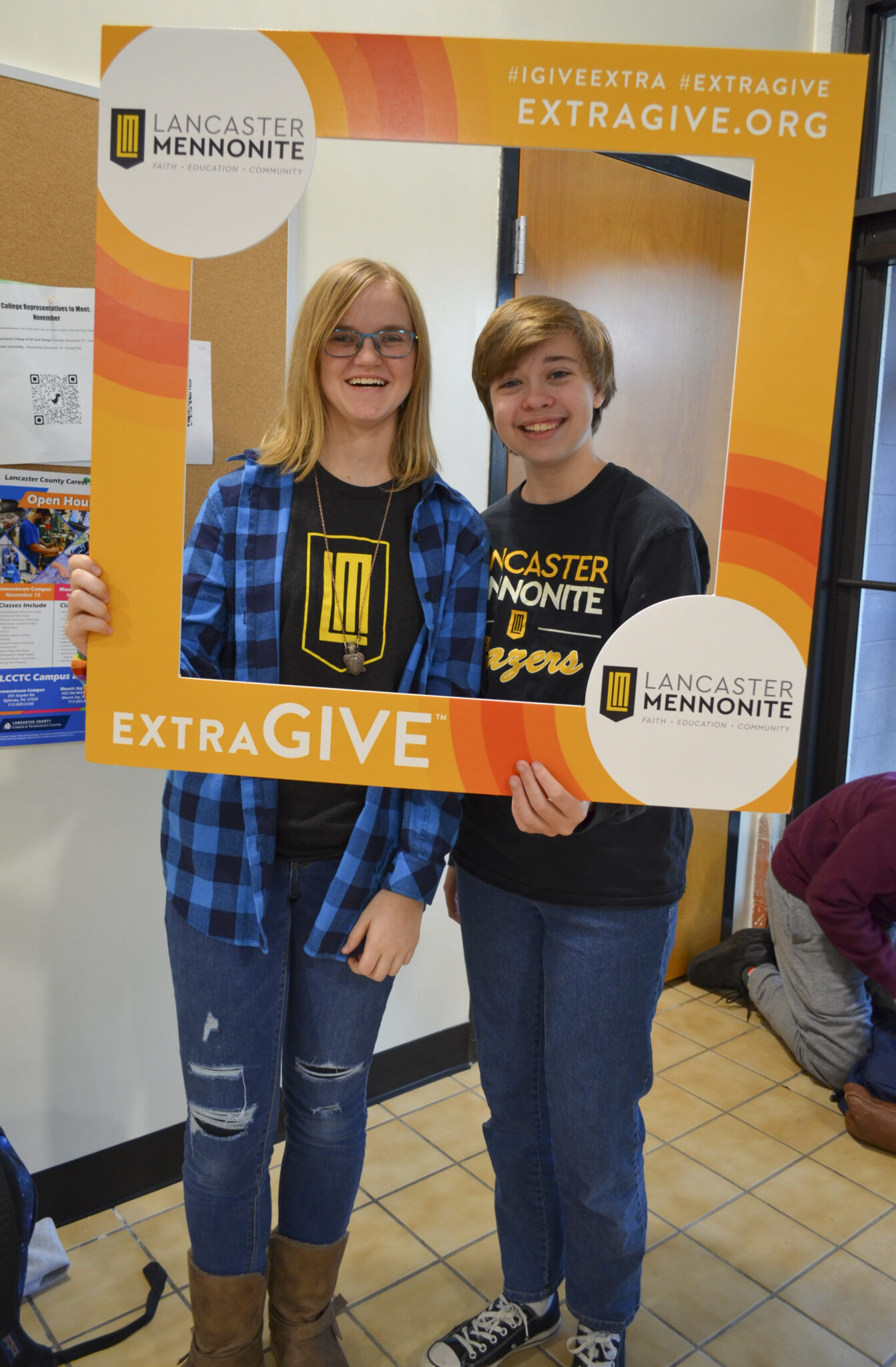 Two LM students in the hallway with Extragive sign.