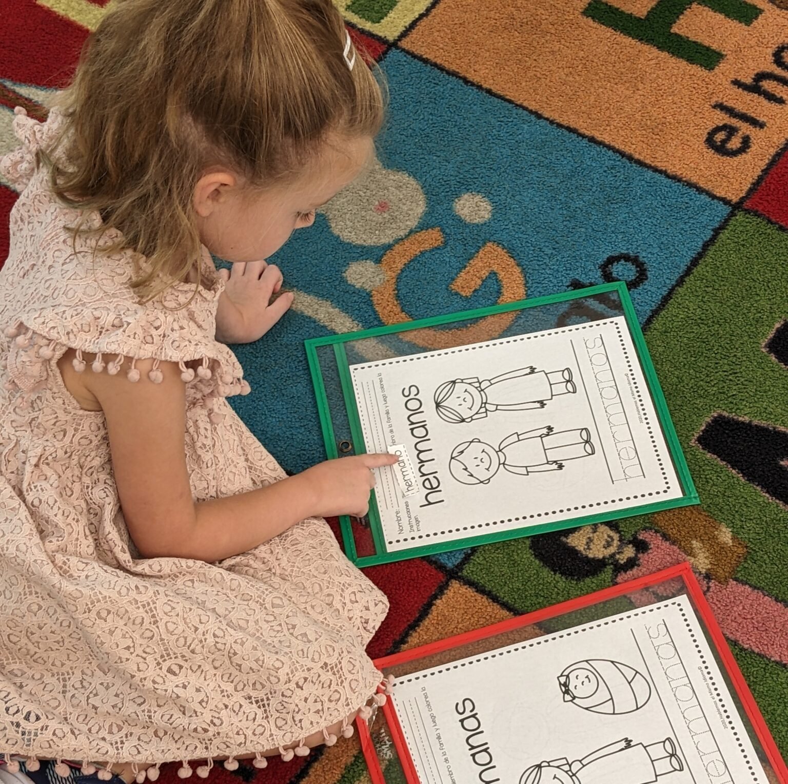 Student learning spanish family words. She is sitting on the floor looking at photos and words of family terms.