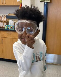 student with goggles and magnifying glass 