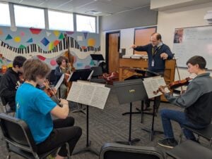 ASSISTANT SUPERINTENDENT, PHIL WARNER WORKING WITH HIGH SCHOOL ORCHESTRA STUDENTS.